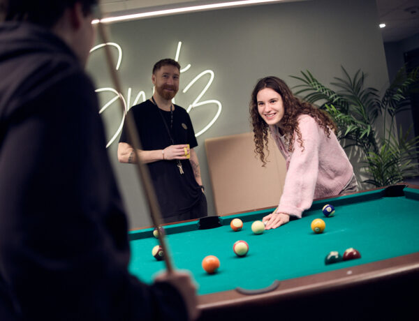 Två elever spelar biljard och en lärare tittar på.