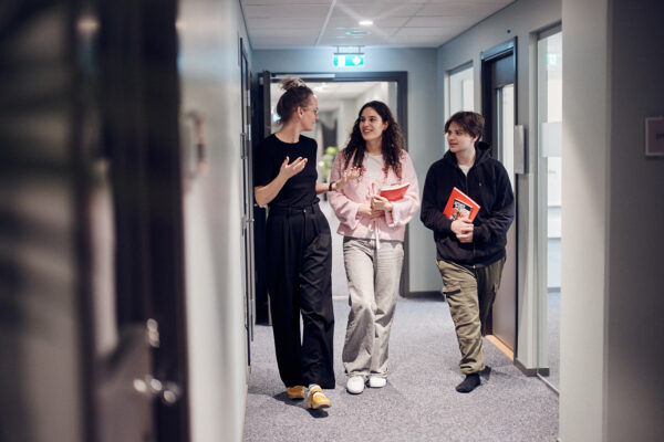 En lärare och två elever pratar och går i skolans korridor.