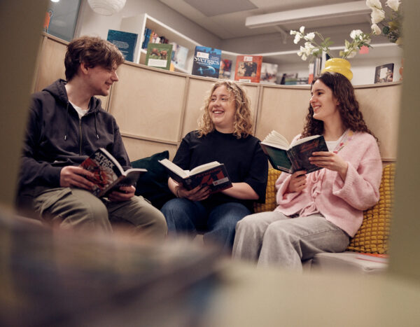 Tre elever som läser tillsammans i biblioteket.