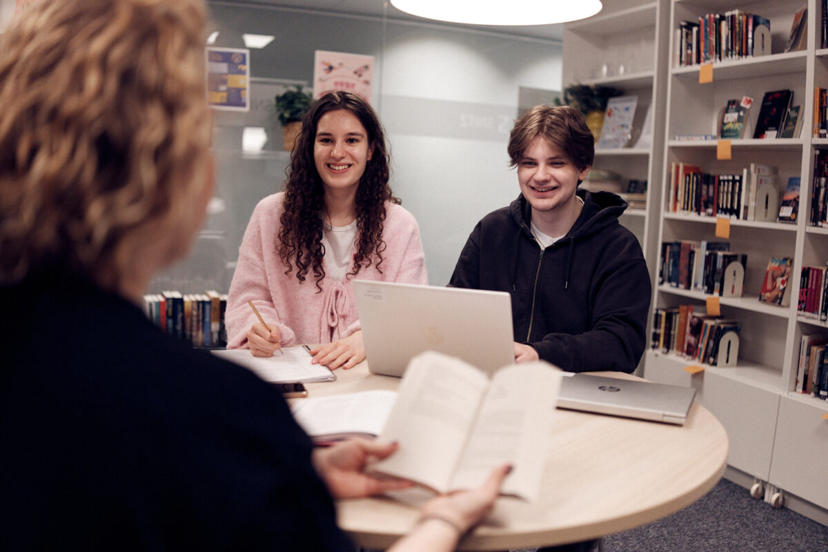 Tre elever som pluggar tillsammans i biblioteket.