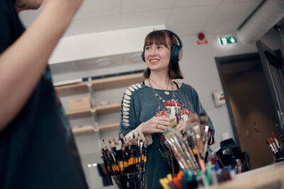 Glad elev med hörlurar framför penslar och färgglada pennor.