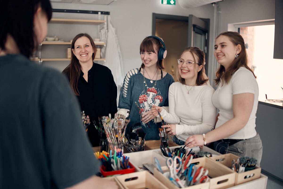 Glada elever och lärare som står framför färgglada färgpennor och penslar.