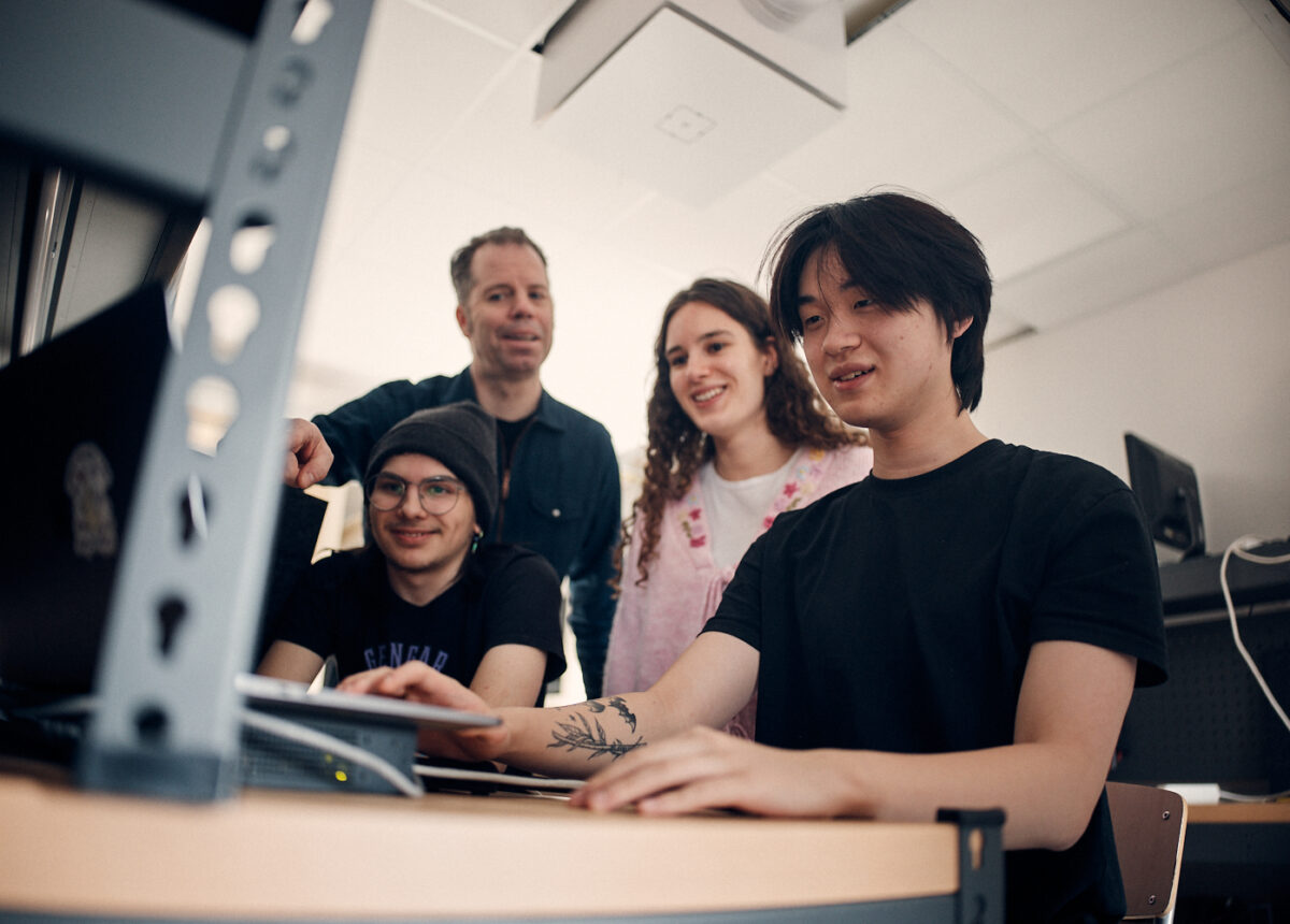 Glada elever och lärare som tittar på när en elev arbetar på dator.