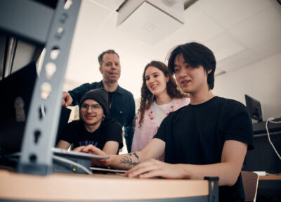 Glada elever och lärare som tittar på när en elev arbetar på dator.