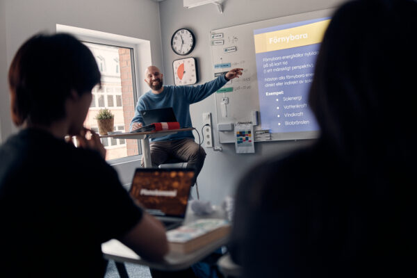 Lärare som undervisar och pekar glatt mot tavlan.