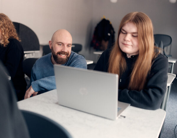 Lärare som hjälper en elev som sitter med dator i klassrummet.