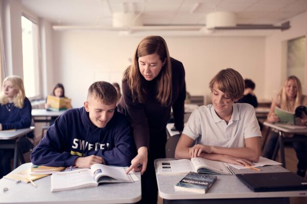 En lärare på Snitz Grundskola hjälper två elever under en lektion. I bakgrunden sitter fler elever.